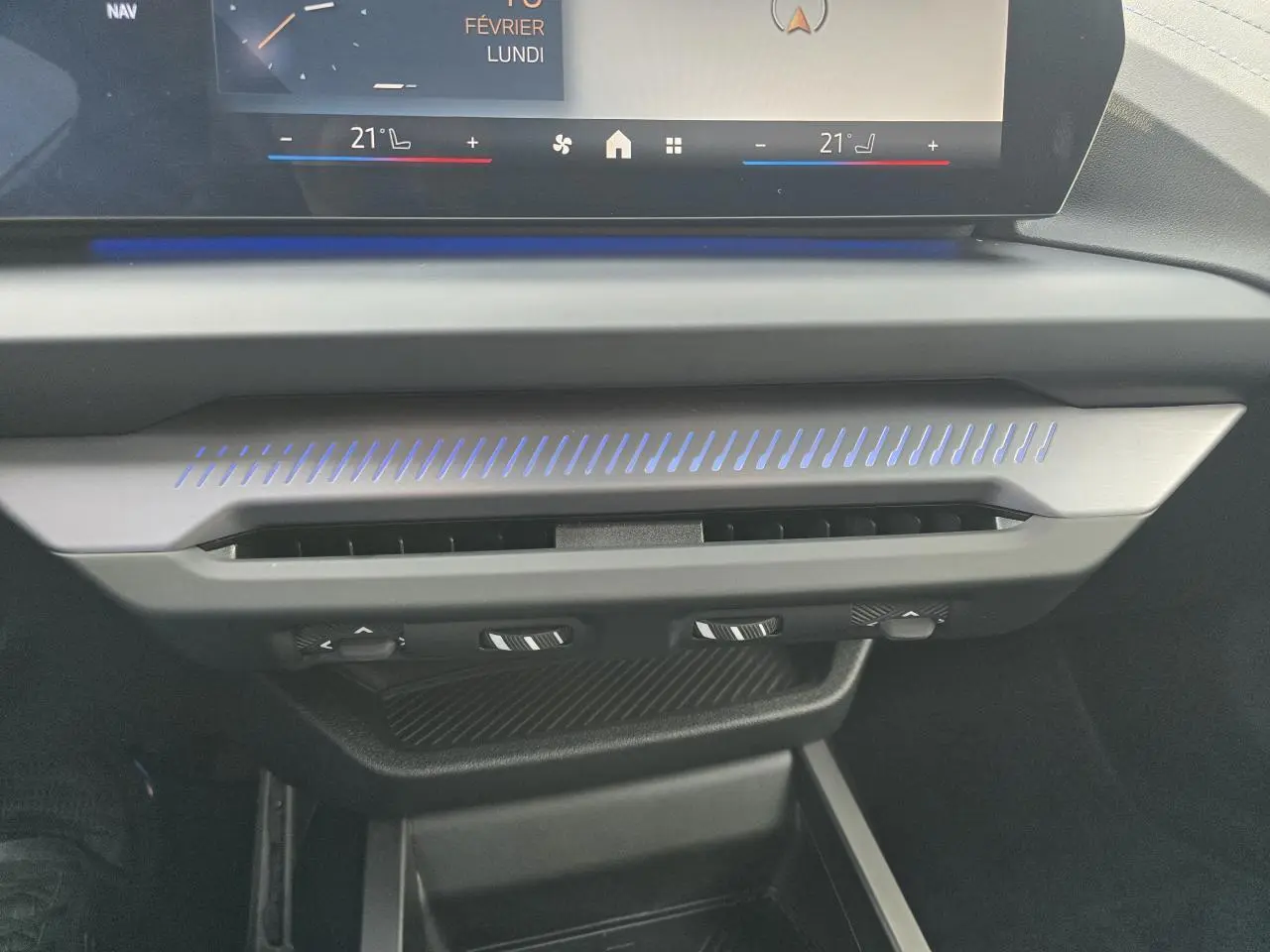 Gros plan sur la console centrale de la BMW Série 1 2025, avec éclairage d'ambiance bleu et commandes de climatisation.