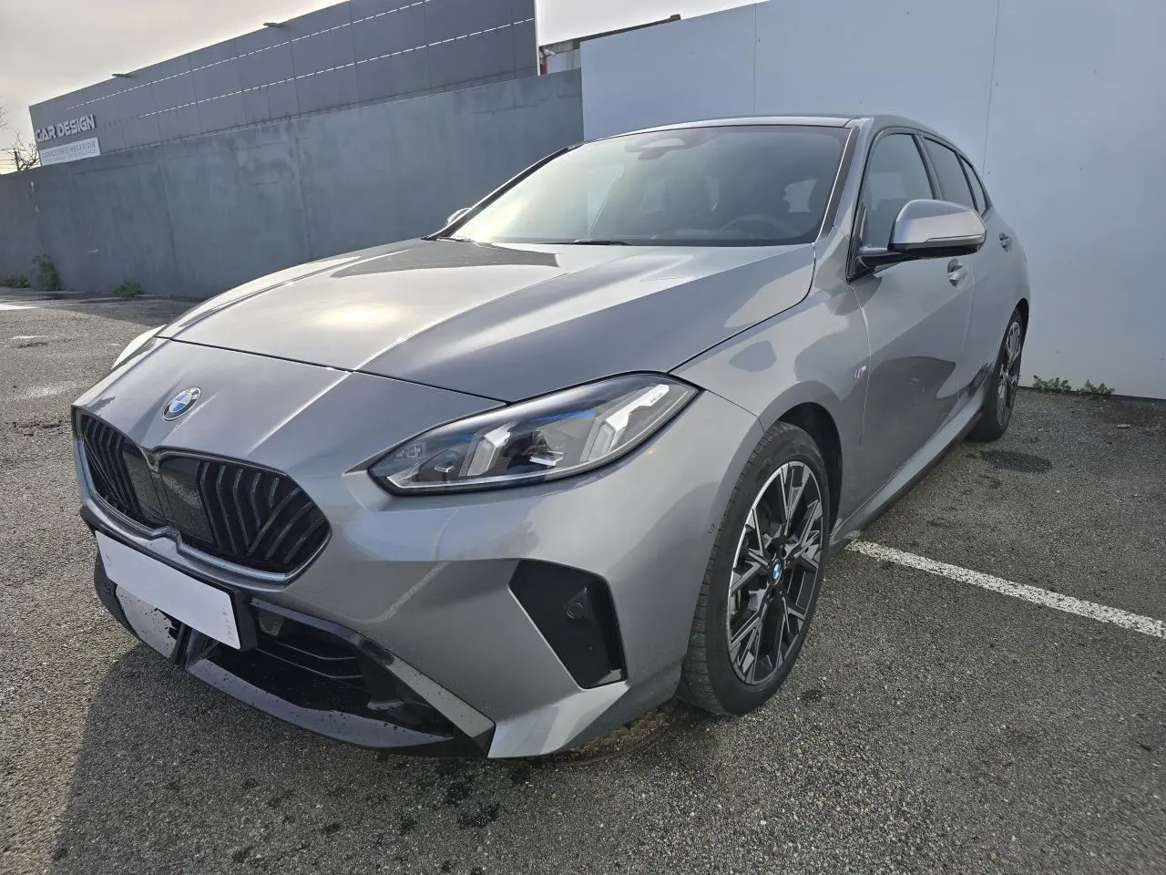 BMW Série 1 gris Skyscraper vue 3/4 avant droit avec calandre noire et jantes alliage 18 pouces M Sport.