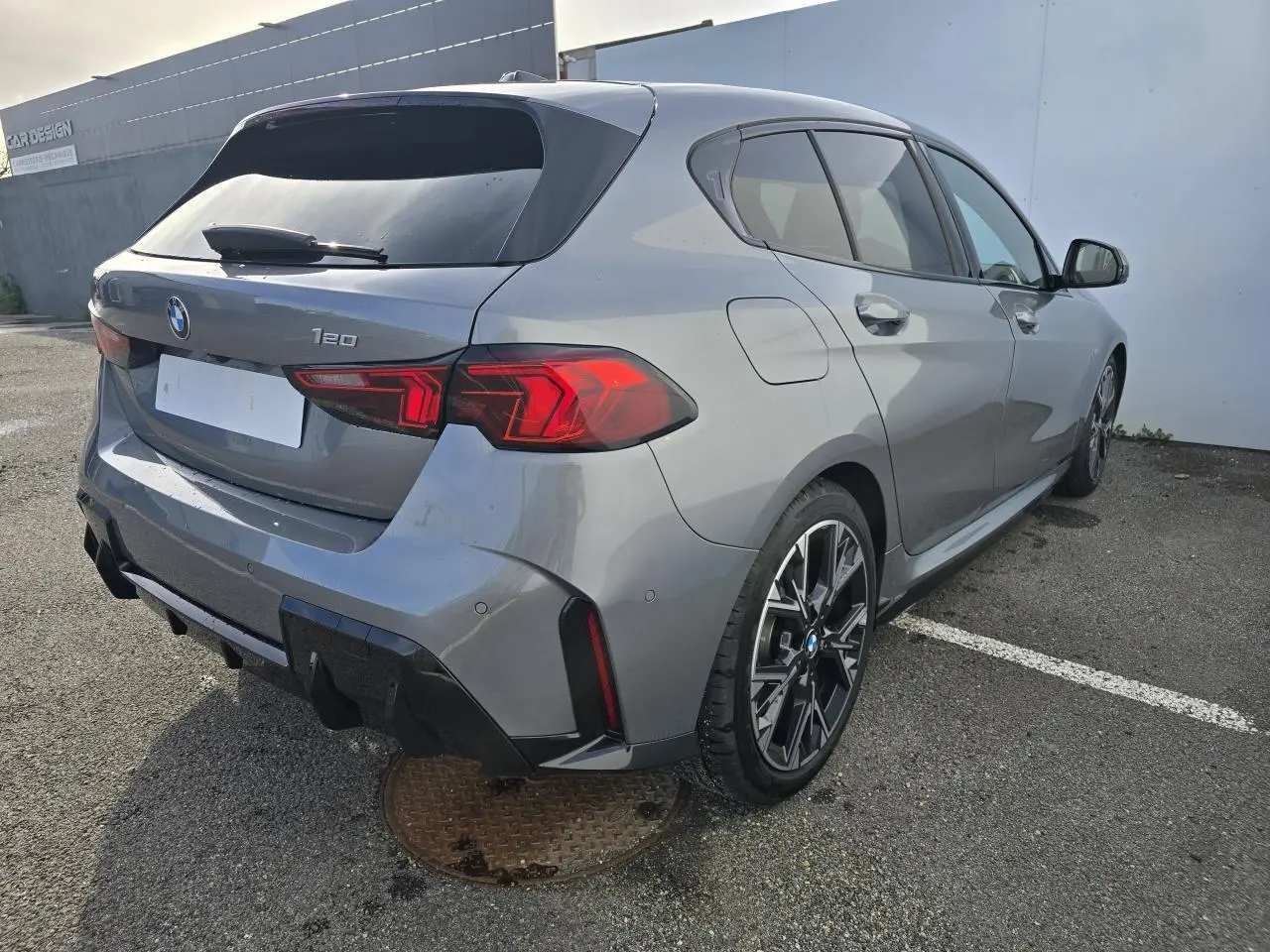 BMW Série 1 gris Skyscraper vue 3/4 arrière droit avec toit noir et jantes M Sport bicolores.