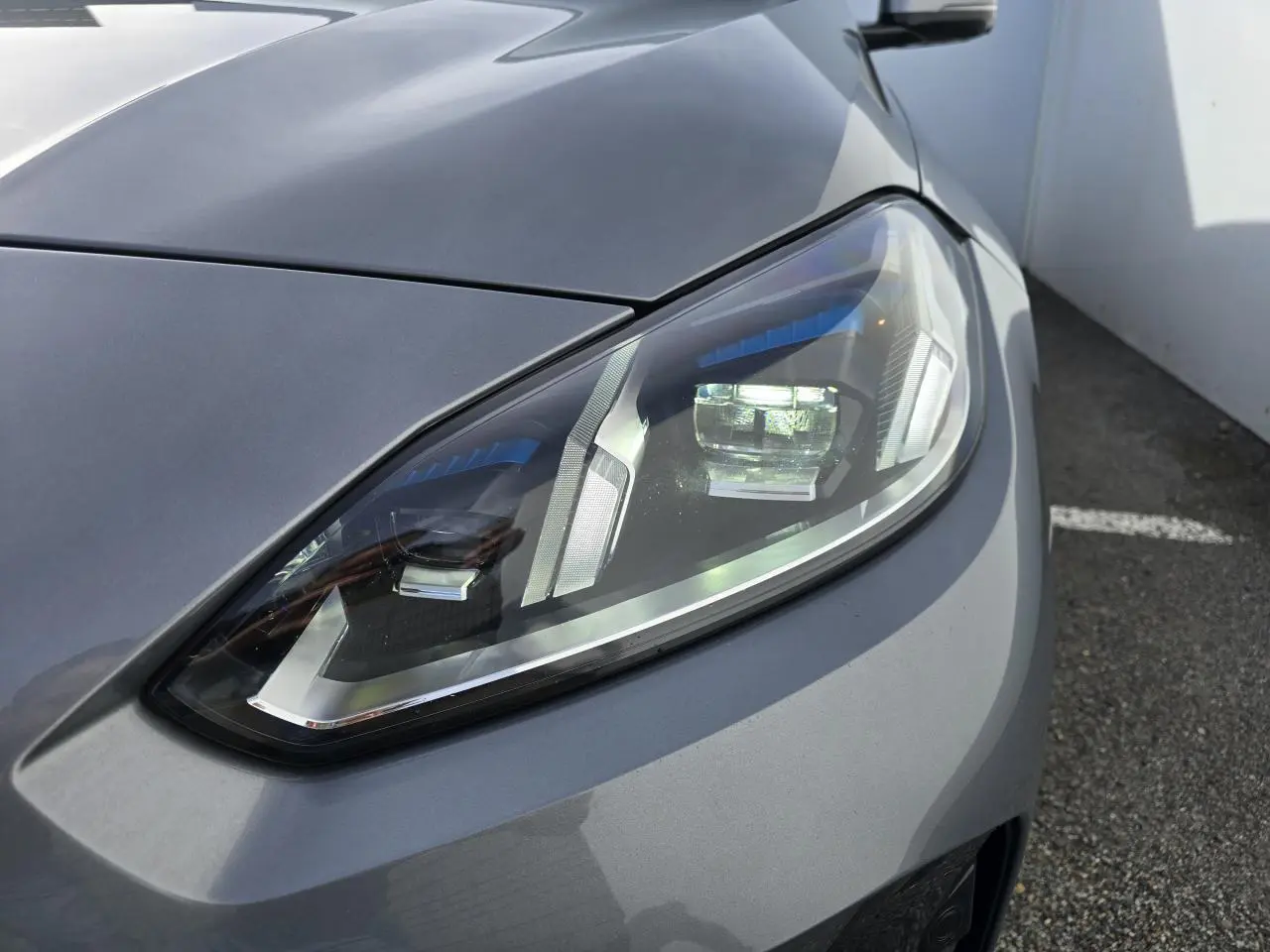 Gros plan sur le phare avant droit de la BMW Série 1 gris Skyscraper avec détails LED et toit noir visible en arrière-plan.