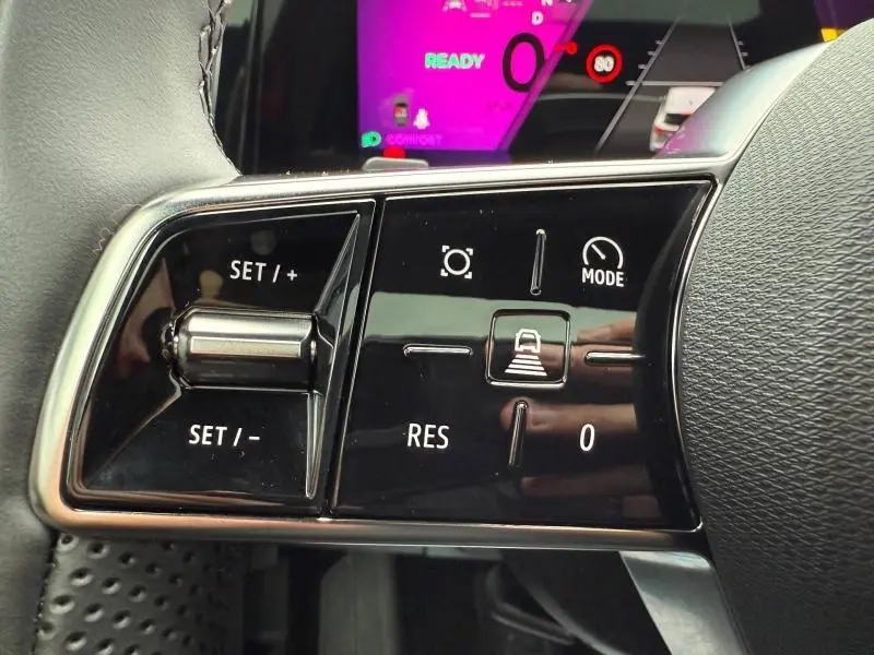 Gros plan sur les commandes noires du volant du Renault Austral rouge, avec boutons de réglage de vitesse et mode.