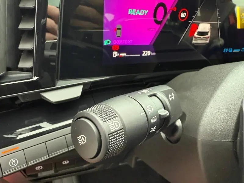 Gros plan sur la commande des phares et le tableau de bord numérique du Renault Austral 2025 hybride, intérieur noir.