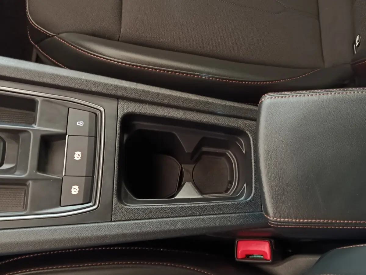 Vue rapprochée de la console centrale noire du CUPRA Formentor 2024 avec porte-gobelets et accoudoir en cuir surpiqué rouge.