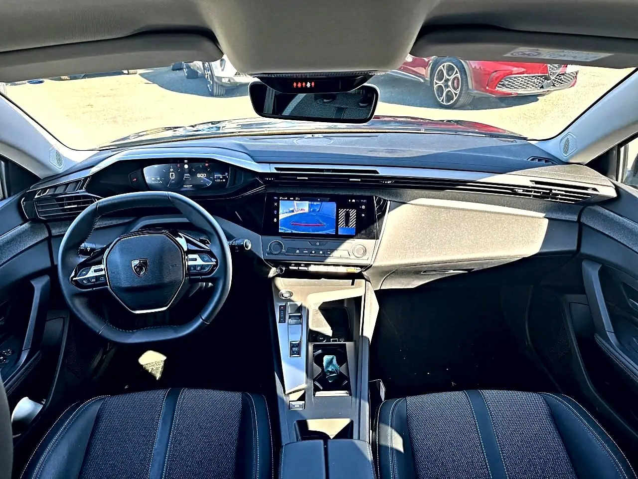 Vue intérieure avant de la Peugeot 308 noire 2025, avec tableau de bord numérique et écran tactile central allumé.