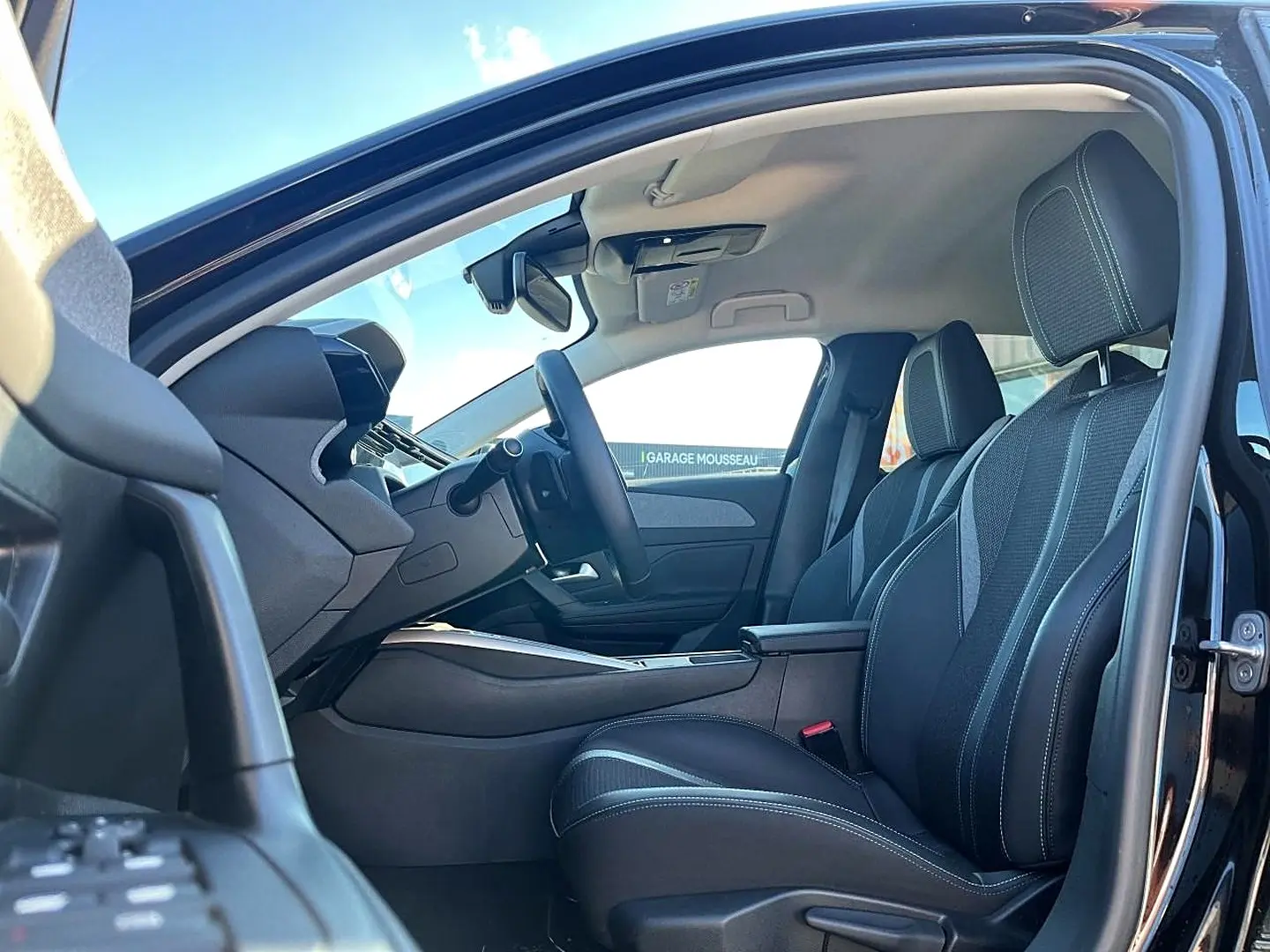 Vue intérieure côté conducteur d'une Peugeot 308 noire 2025, mettant en valeur les sièges et l'accoudoir central.