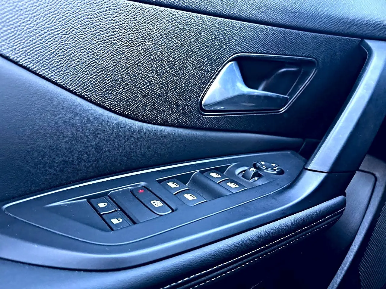 Gros plan sur la commande des vitres et la poignée intérieure côté conducteur de la Peugeot 308 noire, finition Allure.