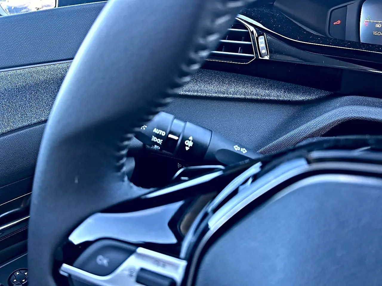 Gros plan sur le volant noir et la commande des phares d'une Peugeot 308 2025, intérieur moderne et épuré.
