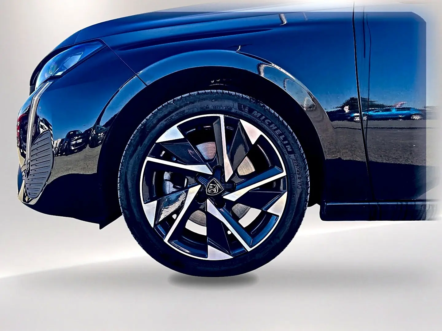 Gros plan sur la roue avant gauche et la jante alu noire et argentée d'une Peugeot 308 noire 2025.