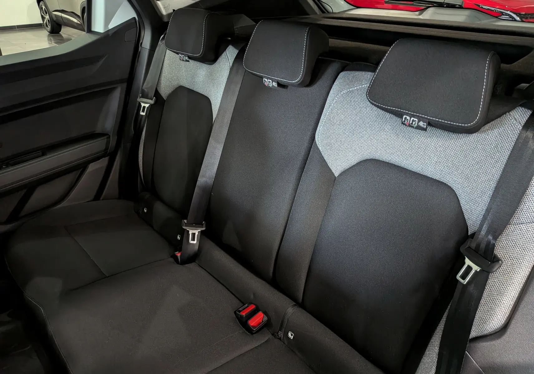 Vue intérieure des sièges arrière noirs et gris du Dacia Duster Hybrid-G 150 CH 4x4 Journey, avec ceintures de sécurité visibles.