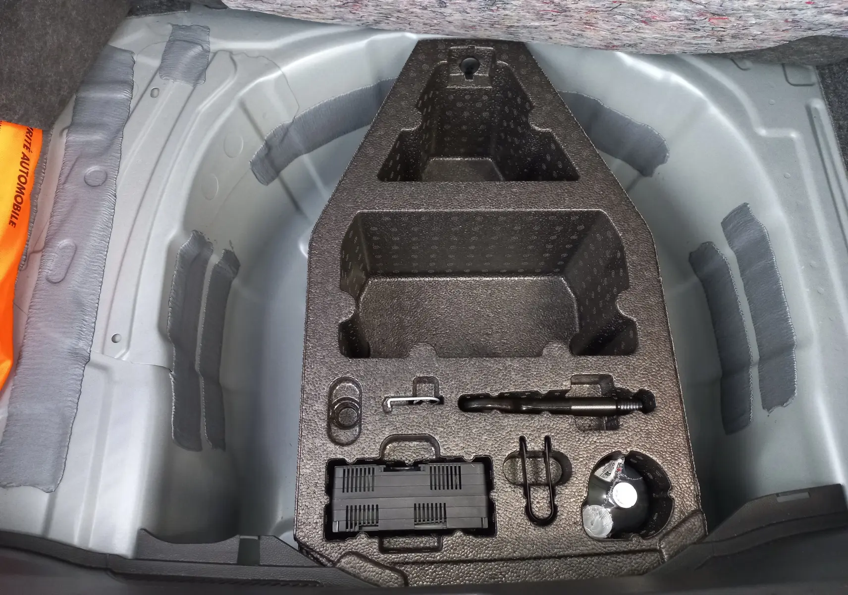 Vue plongeante sur le coffre d’un SEAT Ibiza 2025 gris magnétique, montrant le rangement pour roue de secours et outils intégrés.