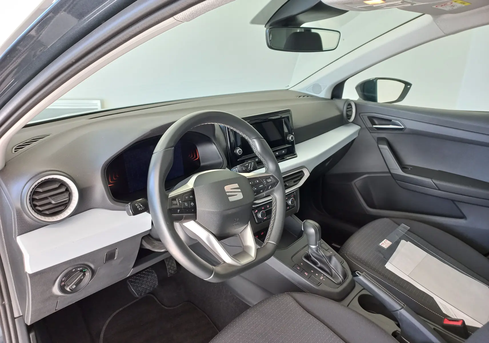 Vue intérieure côté conducteur de la SEAT Ibiza 2025 gris magnétique, avec volant multifonction et console centrale à boîte automatique.