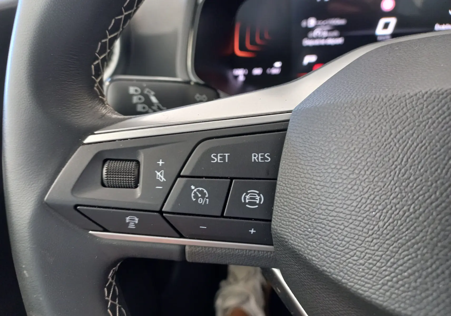 Gros plan sur les commandes au volant côté gauche du SEAT Ibiza 2025 gris magnétique, avec boutons de régulateur de vitesse et assistance.