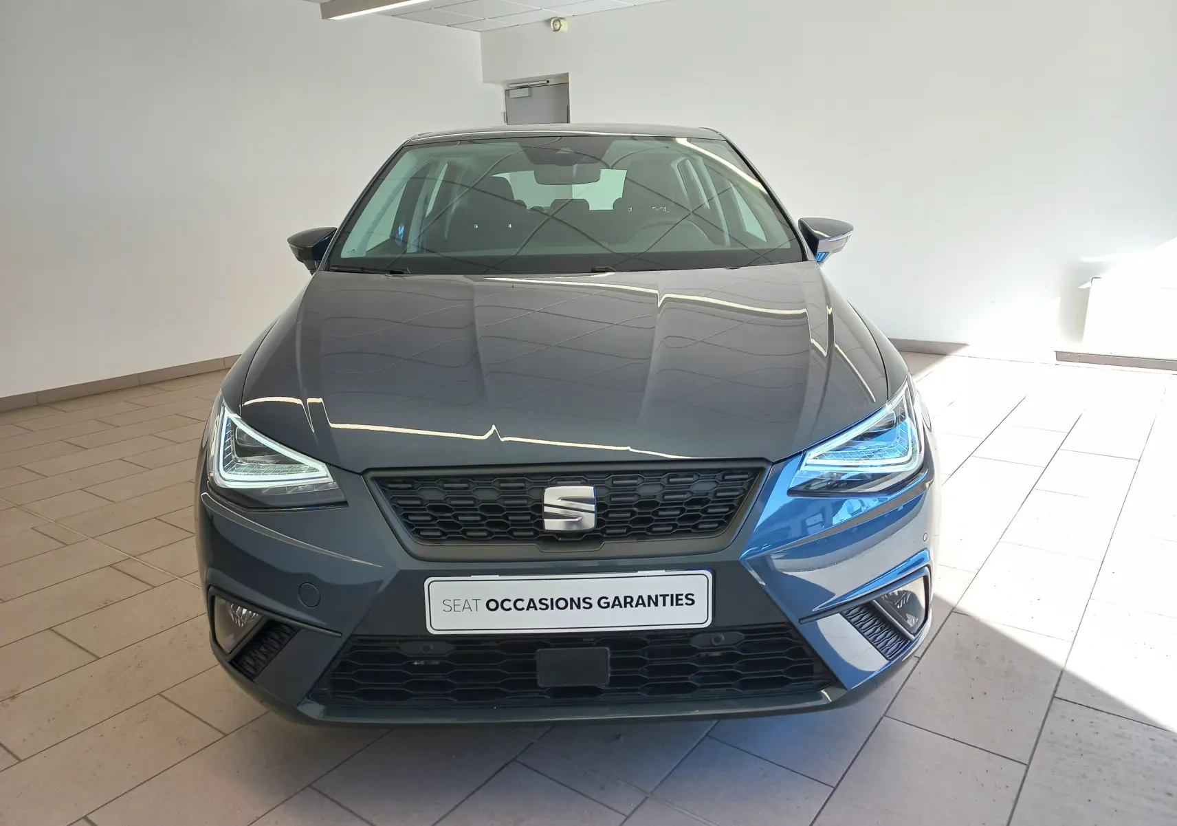Vue frontale d'une SEAT Ibiza 2025 gris magnétique avec phares LED allumés et calandre noire en intérieur showroom.