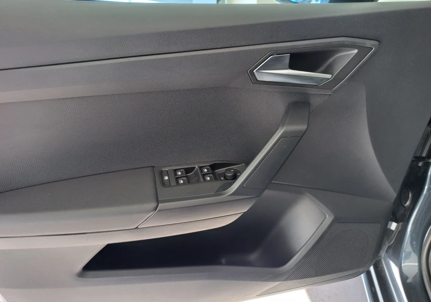Vue intérieure côté gauche de la porte d'une SEAT IBIZA 2025 gris magnétique avec commandes de vitres et poignée noire.