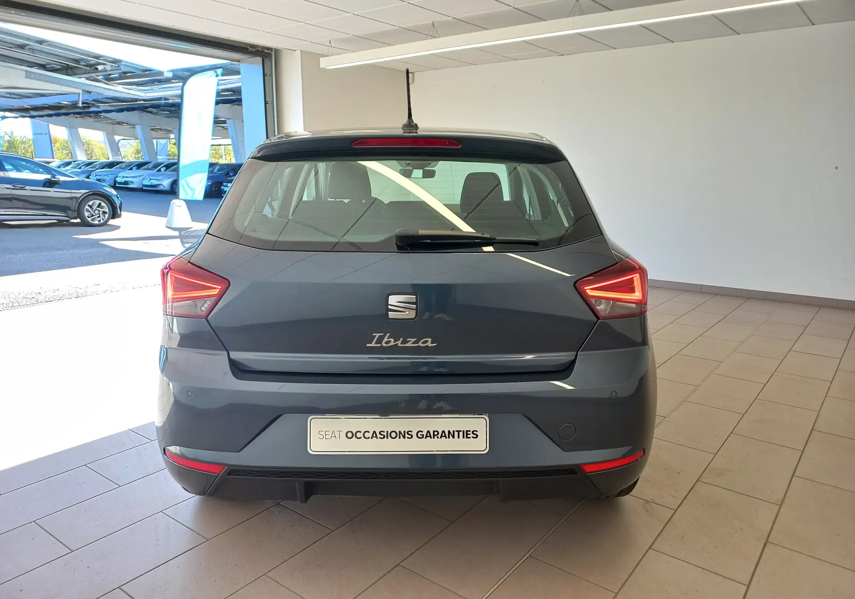 Vue arrière d'une SEAT Ibiza 2025 gris magnétique, avec feux arrière allumés et plaque "SEAT Occasions Garantis" visible.