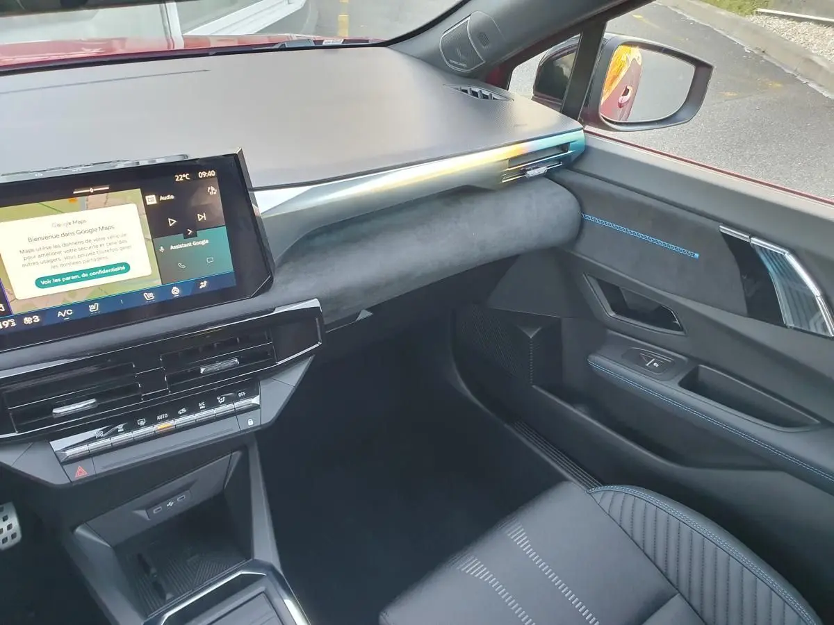 Vue intérieure côté passager de la Renault Clio VI rouge Absolu, avec tableau de bord moderne et écran tactile central.