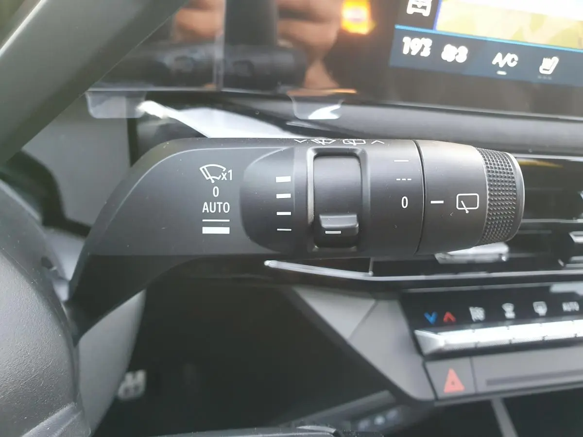 Gros plan sur la commande des essuie-glaces à gauche du volant dans l’habitacle de la Renault Clio VI rouge Absolu.