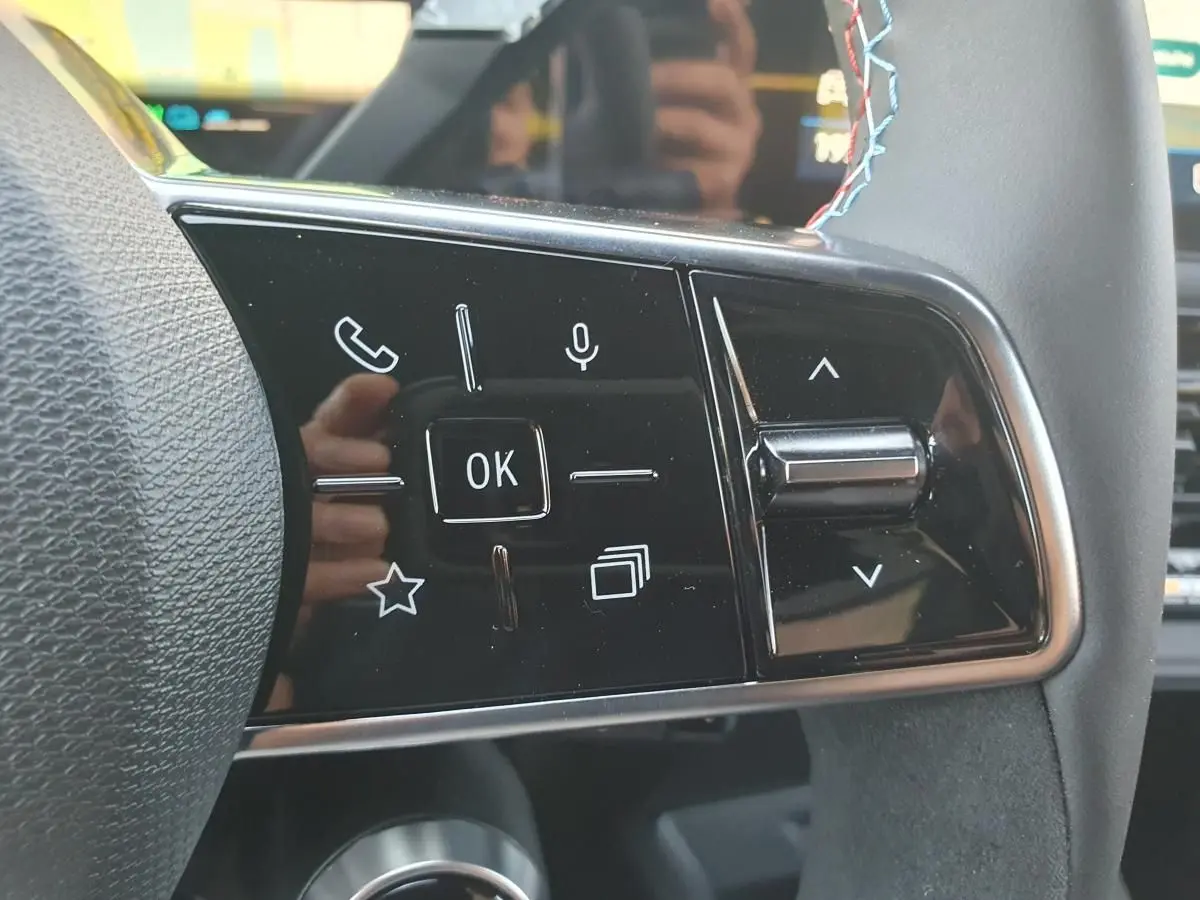 Gros plan sur les commandes multifonctions du volant de la Renault Clio VI, finition Esprit Alpine, avec surpiqûres bleues.