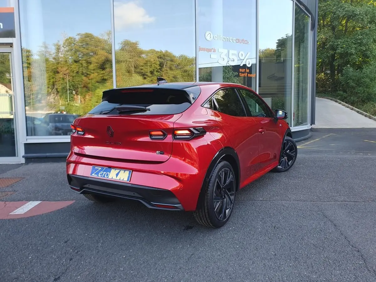Vue 3/4 arrière droite de la Renault Clio VI rouge Absolu avec jantes alliage noires et toit noir brillant.