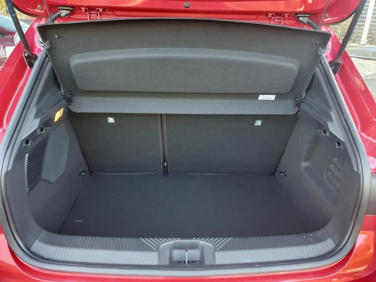 Coffre ouvert de la Renault Clio VI rouge absolu, vue arrière montrant l’espace de chargement vide et la tablette cache-bagages.