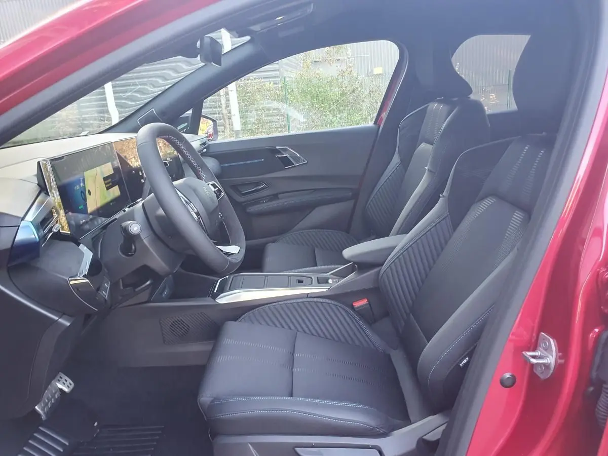 Vue intérieure côté conducteur de la Renault Clio VI rouge Absolu, sièges noirs et tableau de bord numérique.