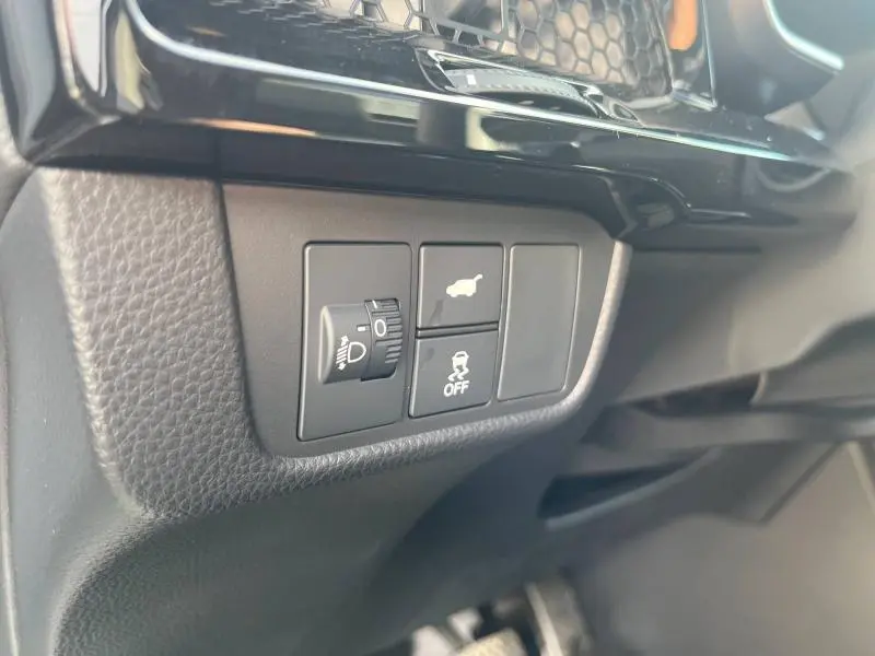 Gros plan sur les commandes noires du tableau de bord côté conducteur du Honda CR-V 2024, avec réglage des phares et bouton de stabilité.