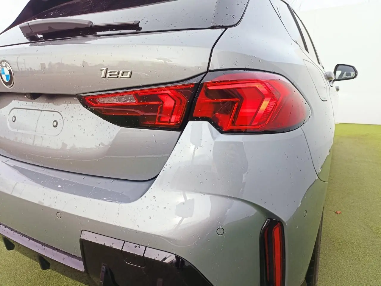 Vue 3/4 arrière droit d'une BMW Série 1 120 M Sport gris Skyscraper avec toit noir et feux arrière LED distinctifs.