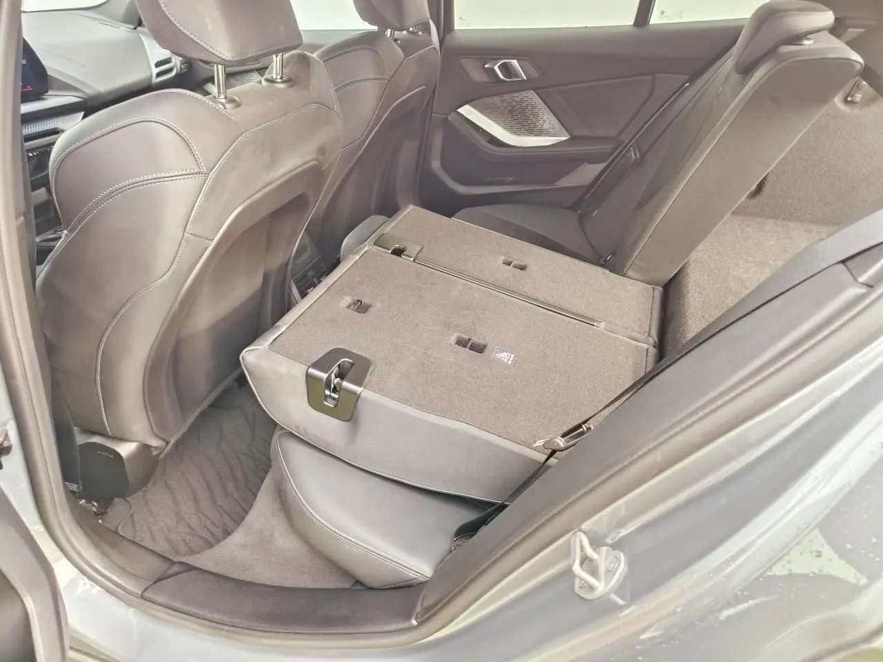 Vue côté droit de l’intérieur arrière de la BMW Série 1 gris Skyscraper, banquette rabattue et sellerie noire.