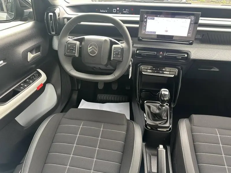 Vue intérieure avant centrée sur le volant et la console centrale d'une Citroën C3 2025 avec sellerie noire et écran tactile.