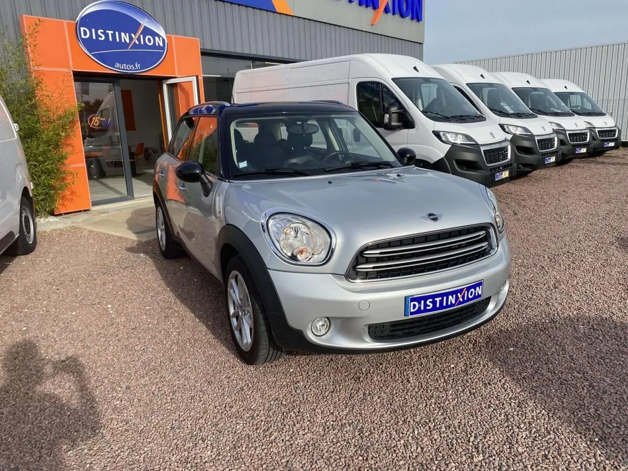 MINI Countryman gris clair en 3/4 avant droit avec toit noir et calandre chromée, stationnée devant un concessionnaire.