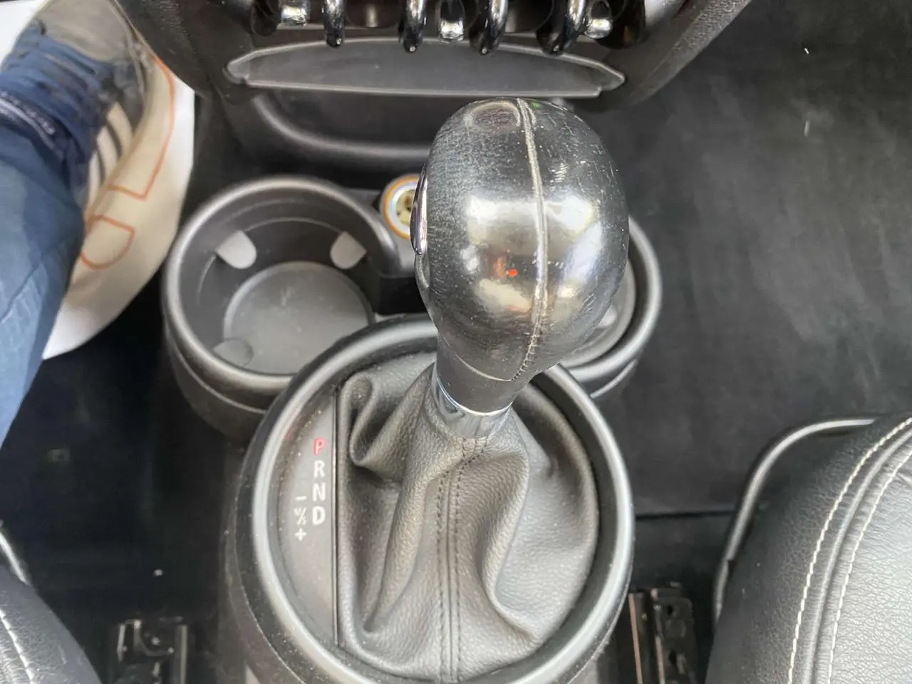 Le levier de vitesses automatique en cuir noir du MINI Countryman gris clair vu de dessus, avec porte-gobelets adjacent.