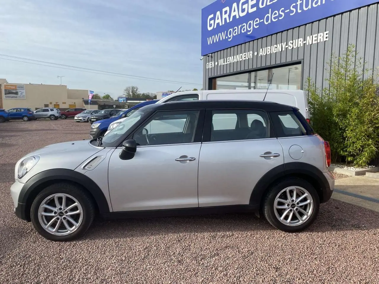 Vue de profil côté gauche d'une MINI Countryman gris clair avec toit noir, roues alliage et rétroviseurs noirs.