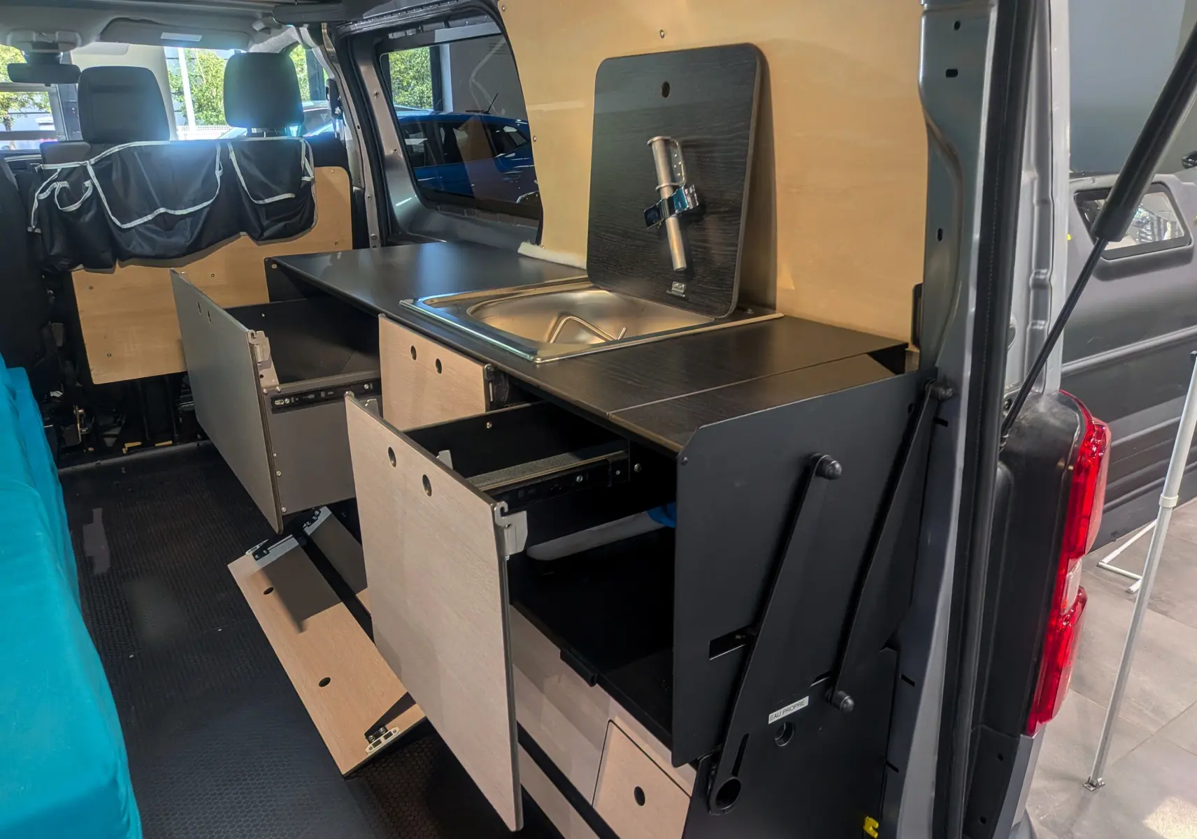 Vue intérieure côté droit du Peugeot Expert Fourgon gris acier aménagé avec cuisine intégrée en bois et rangements ouverts.