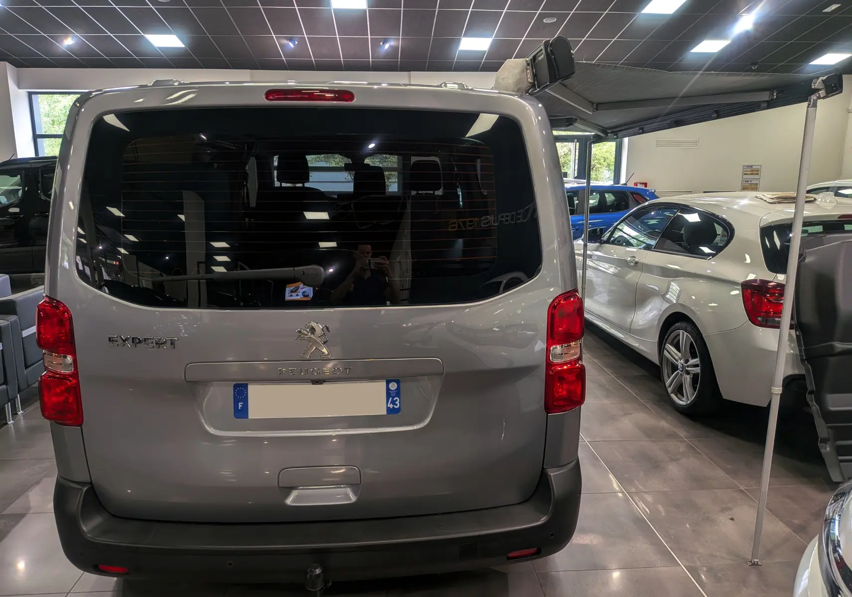 Vue arrière du Peugeot Expert Fourgon gris acier 2023 avec store latéral déployé en intérieur showroom.