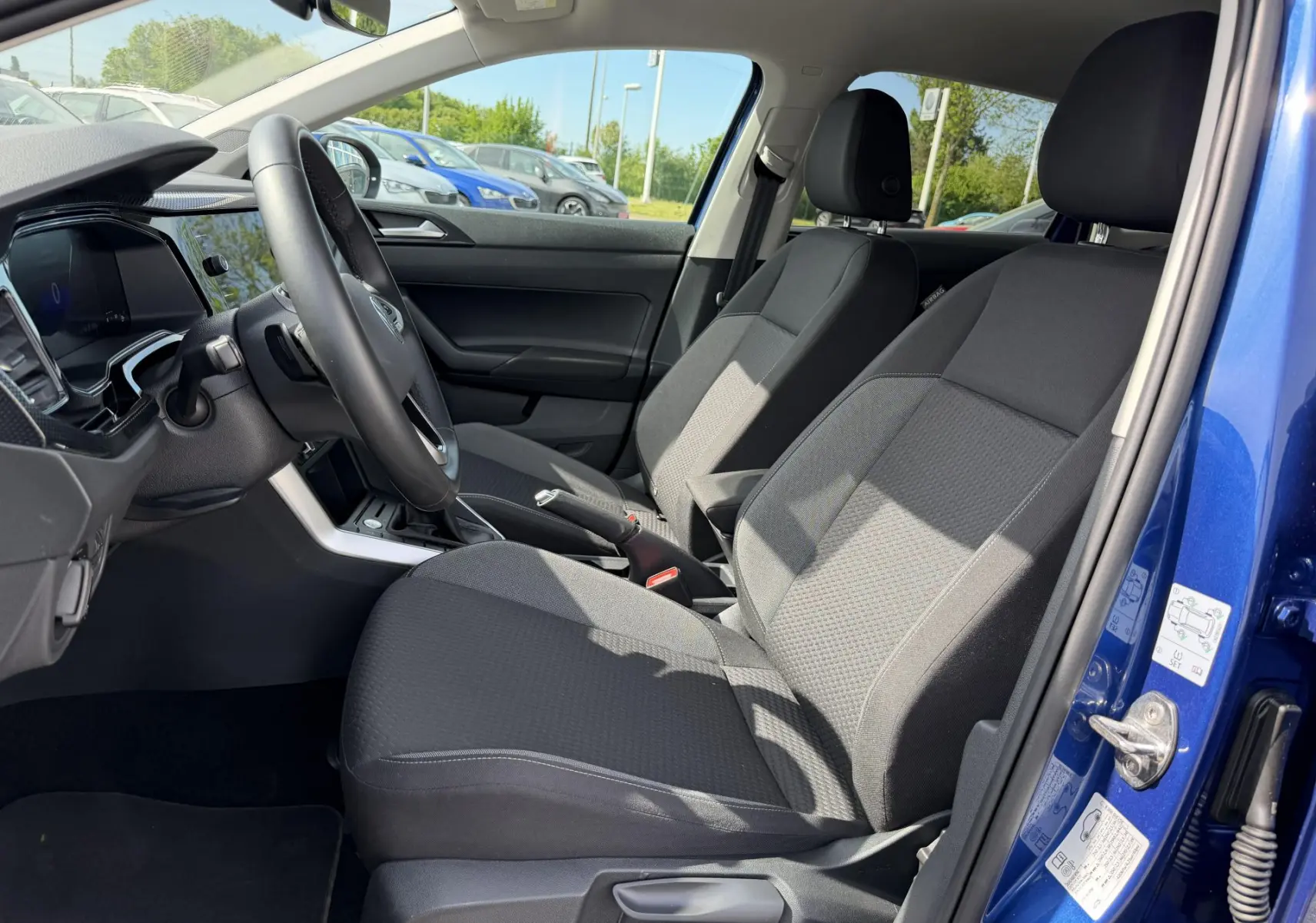 Vue intérieure côté conducteur du Volkswagen Taigo bleu 2025, montrant les sièges avant et le volant multifonctions.