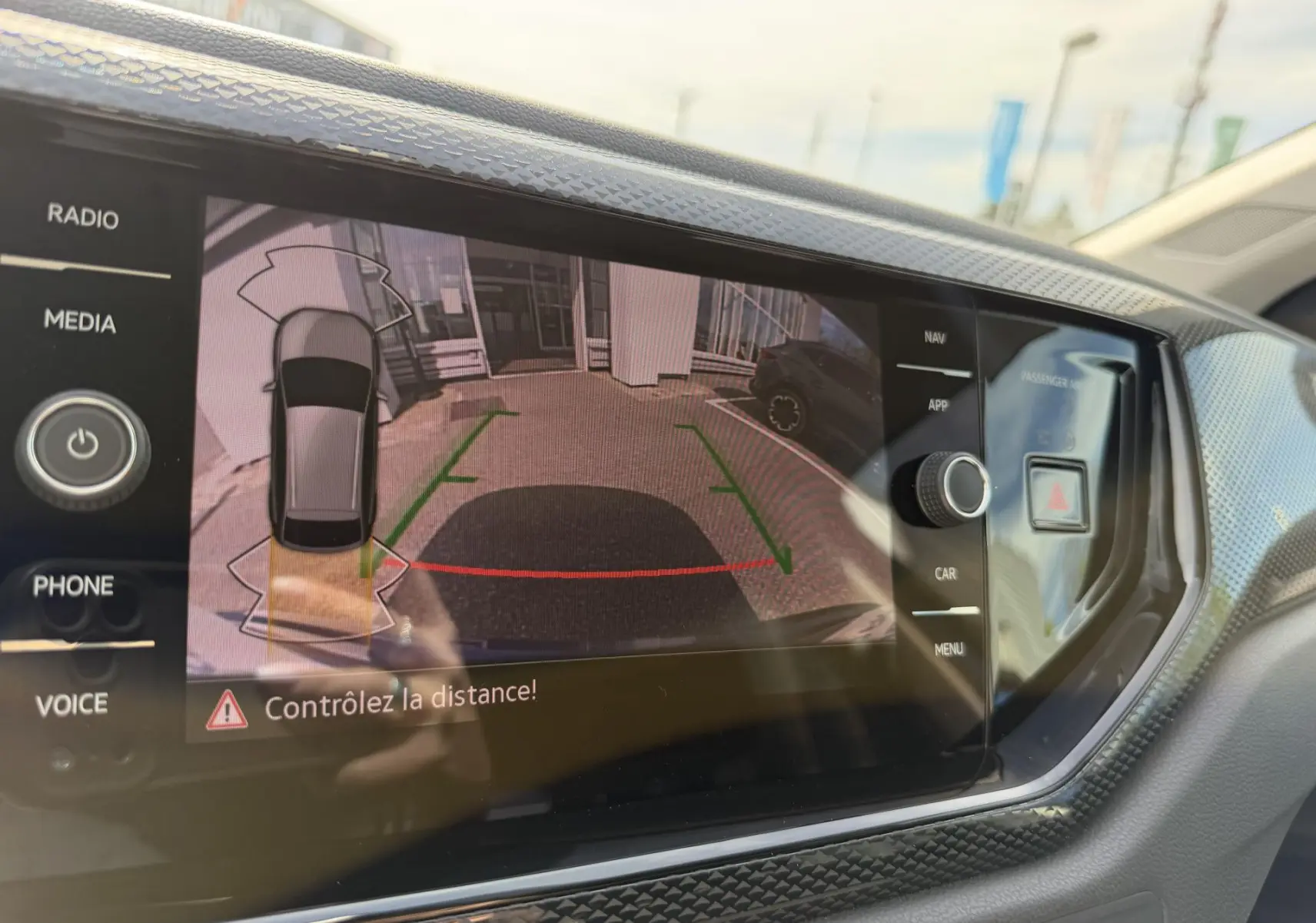 Écran tactile intérieur montrant la caméra de recul du Volkswagen Taigo bleu avec aides au stationnement activées.
