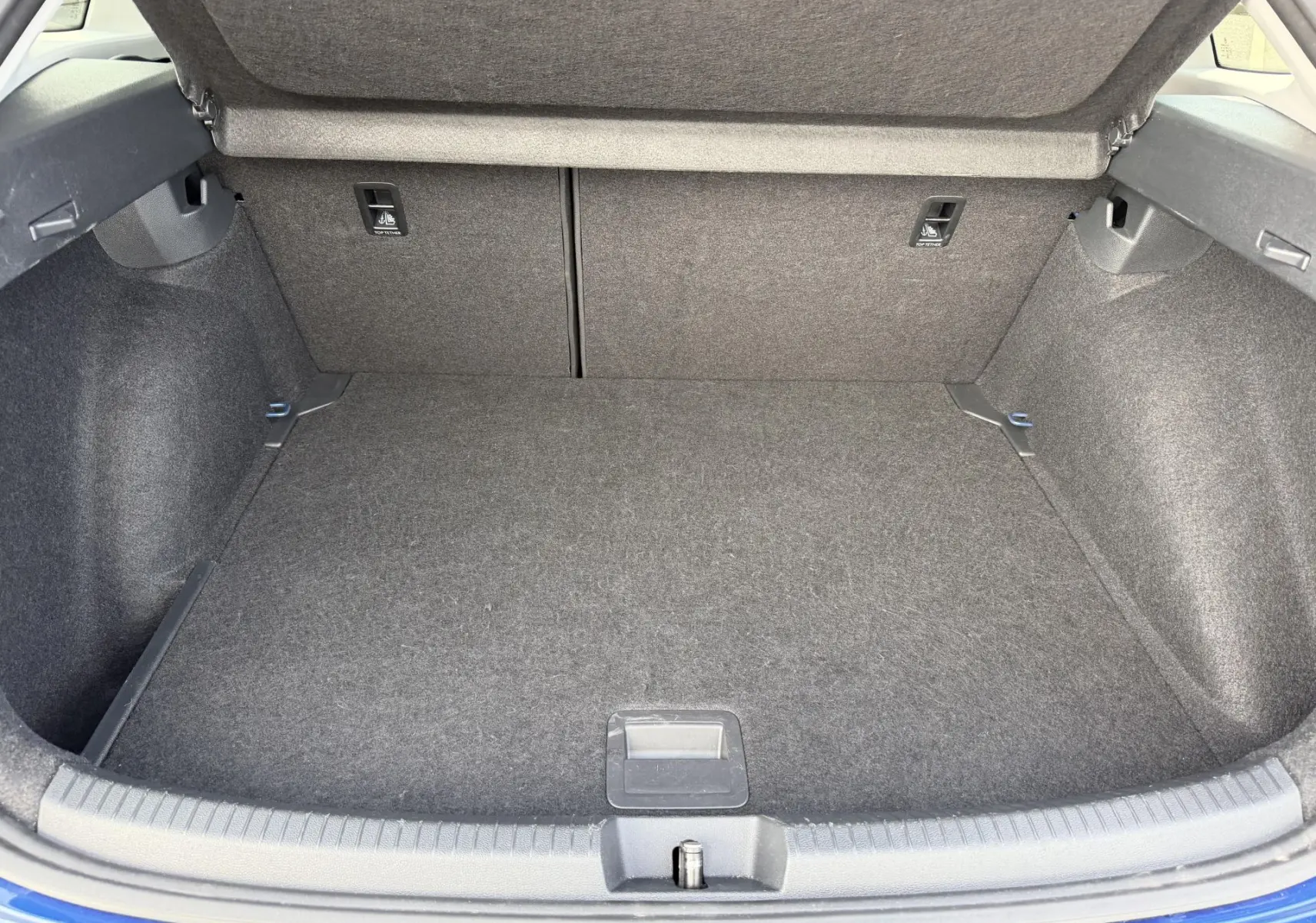 Coffre ouvert vu de l'arrière d'un Volkswagen Taigo bleu, montrant un espace de chargement propre et tapissé de tissu gris.