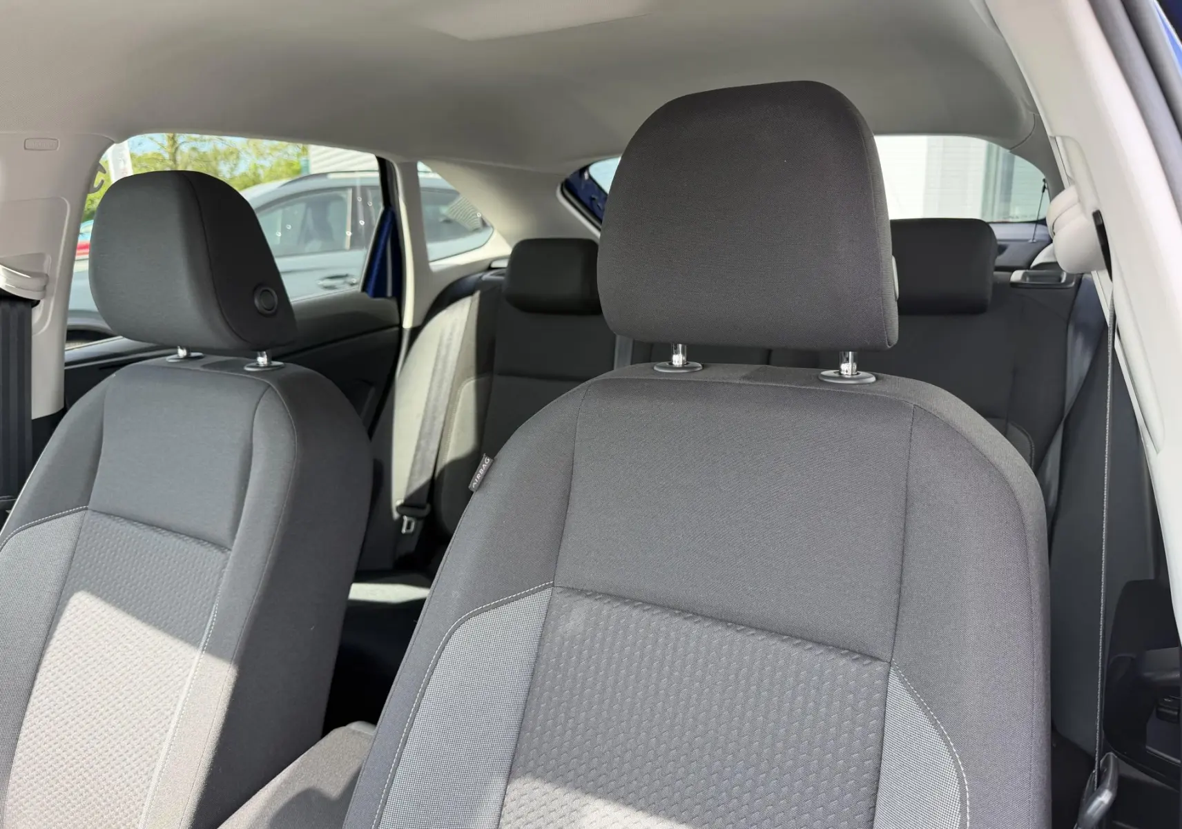 Vue intérieure des sièges avant et arrière en tissu gris du Volkswagen Taigo bleu, avec lumière naturelle entrant par la porte ouverte.