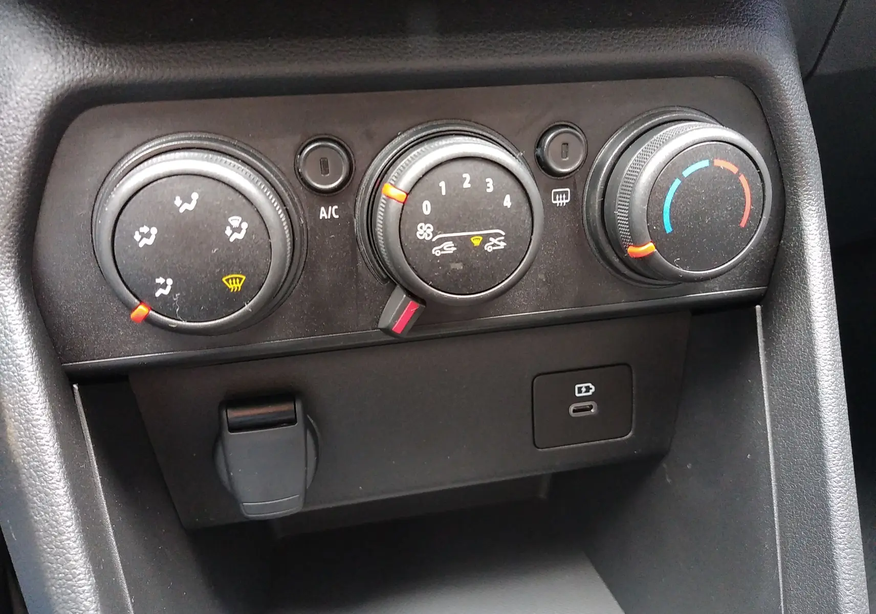 Panneau de commande de climatisation avec trois molettes et port USB dans une Dacia Sandero bleu Iron 2025.