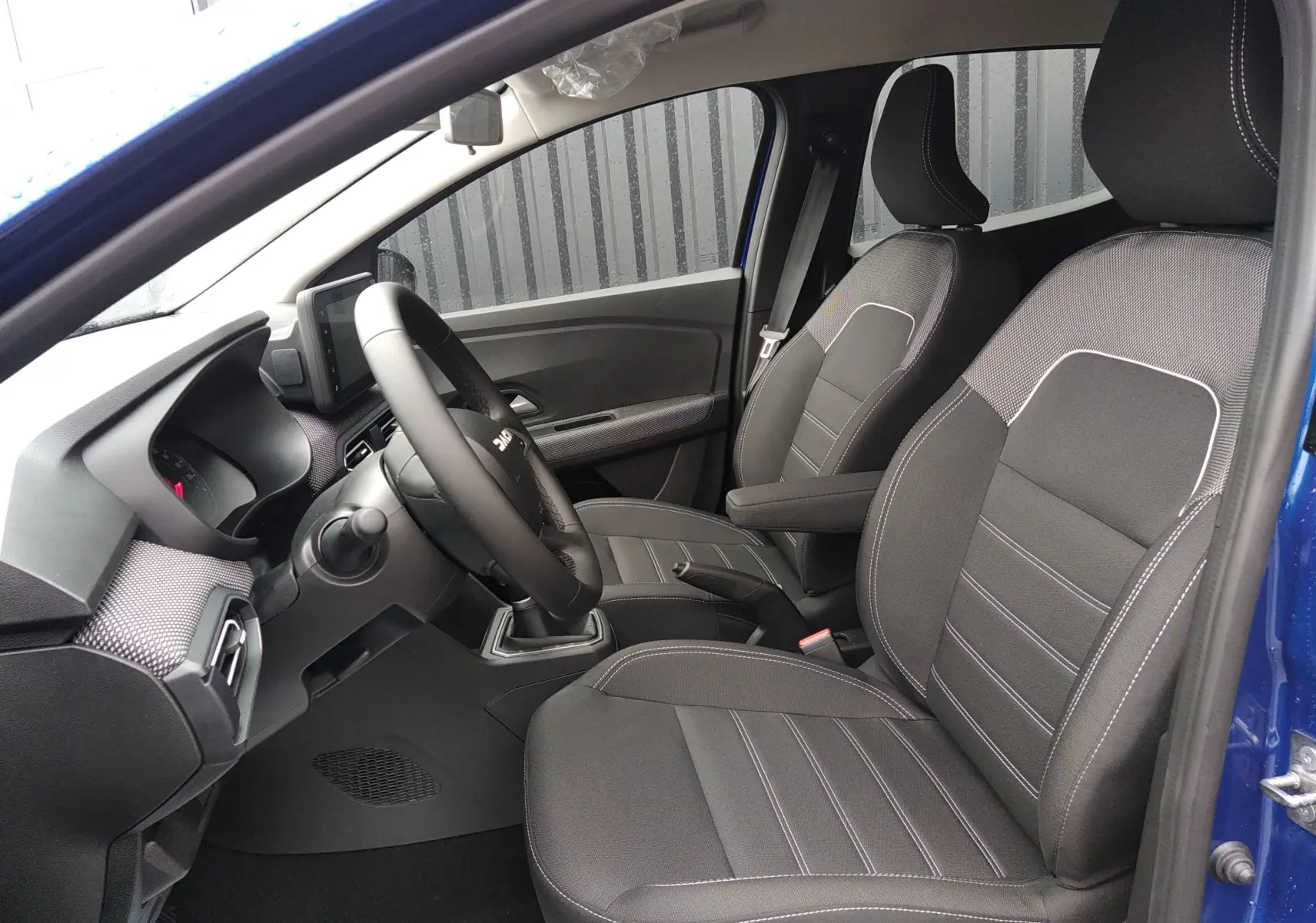 Vue intérieure côté gauche de la Dacia Sandero 2025 bleu iron, montrant les sièges tissu noirs et le tableau de bord moderne.