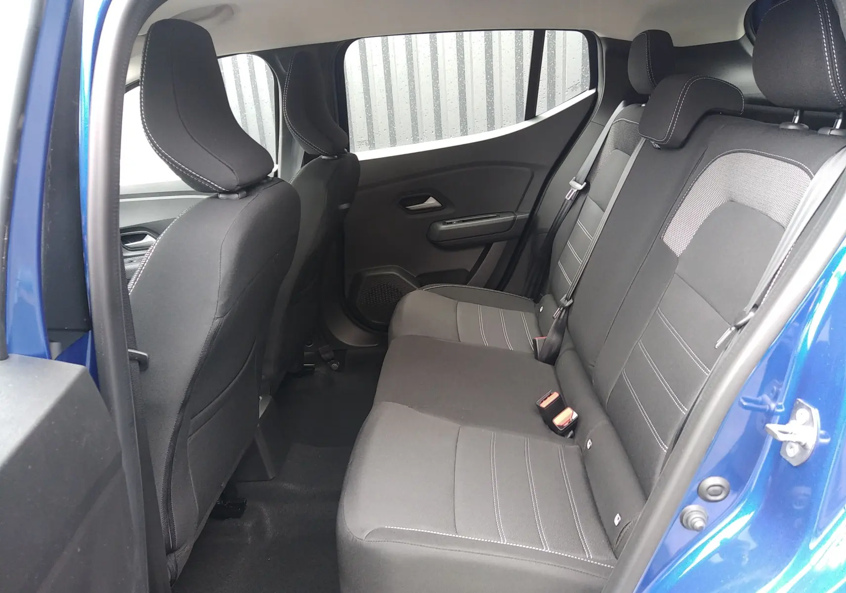 Vue intérieure côté droit sur les sièges arrière en tissu gris de la Dacia Sandero 2025 bleu Iron avec ceinture de sécurité.