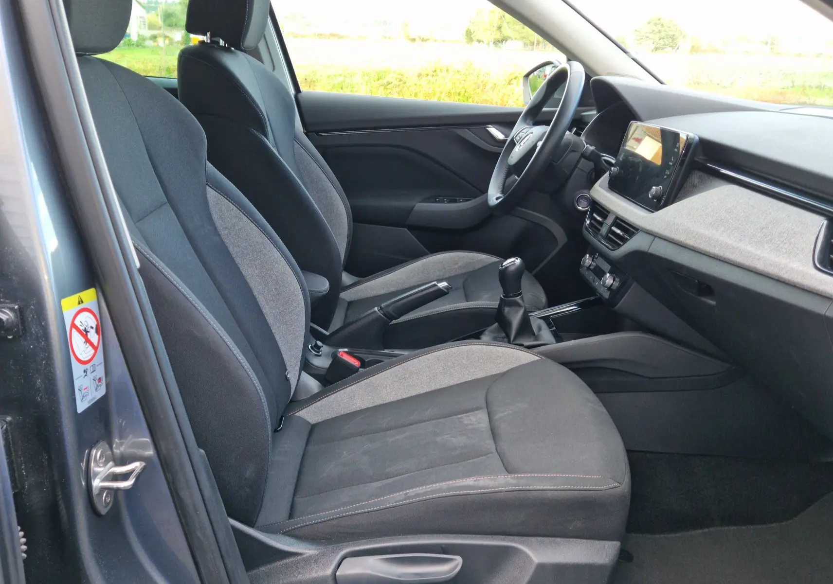 Vue intérieure côté conducteur du Skoda Kamiq gris graphite métal 2024 avec sièges tissu gris et console centrale moderne.