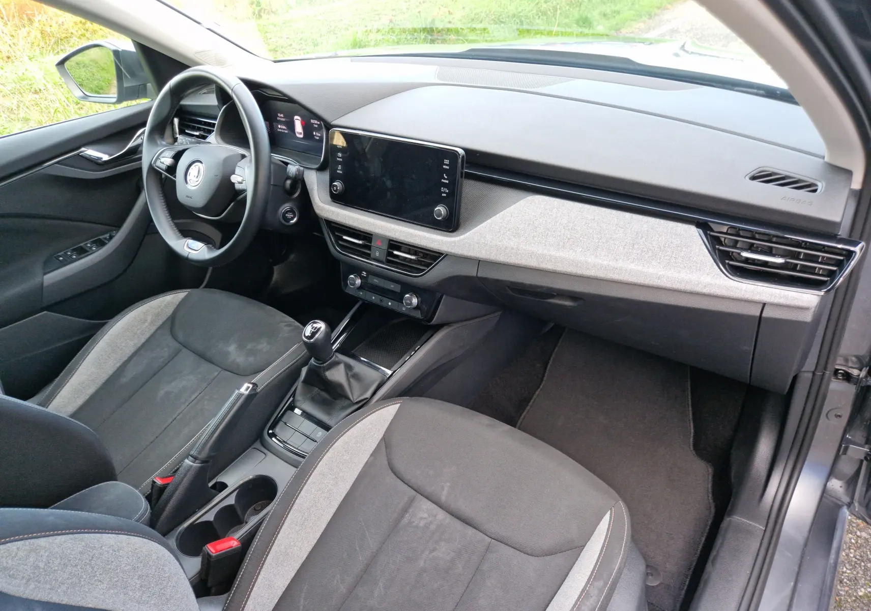 Intérieur du Skoda Kamiq 2024 en gris graphite, vue côté conducteur montrant tableau de bord et sièges tissu gris/noir.