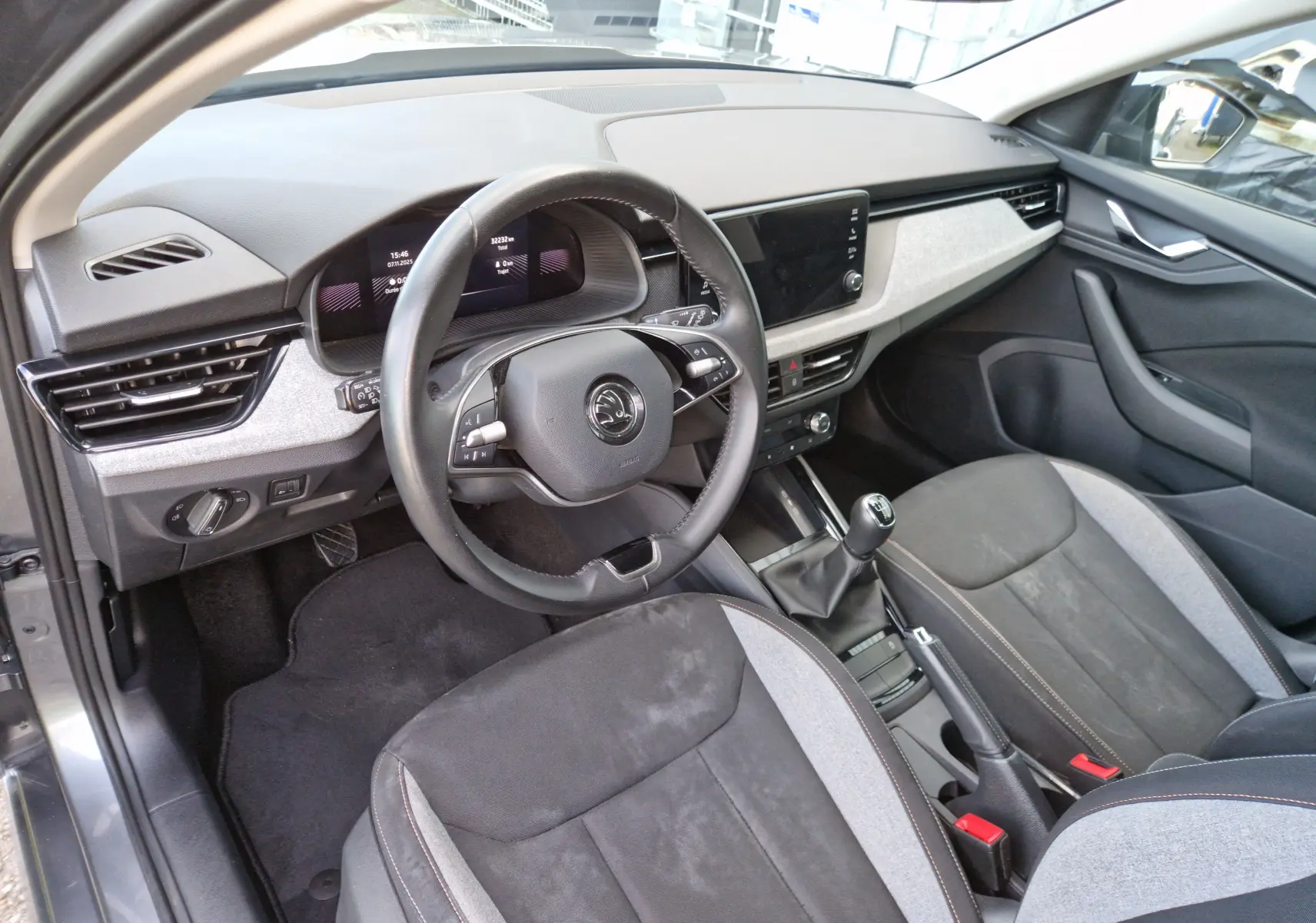 Intérieur avant droit du Skoda Kamiq gris graphite 2024, volant cuir, tableau de bord digital et sièges tissu gris/noir.