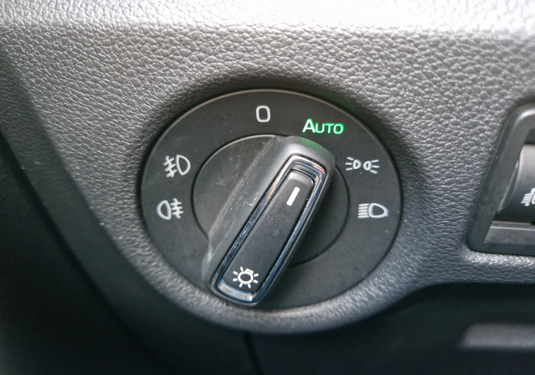 Gros plan sur le sélecteur de phares noir du Skoda Kamiq 2024 gris graphite, affichant le mode automatique activé en vert.