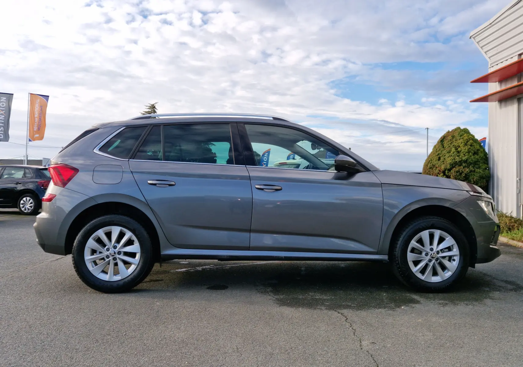 Profil côté gauche d'un Skoda Kamiq gris graphite métal 2024, avec jantes alliage et toit ouvrant visible.