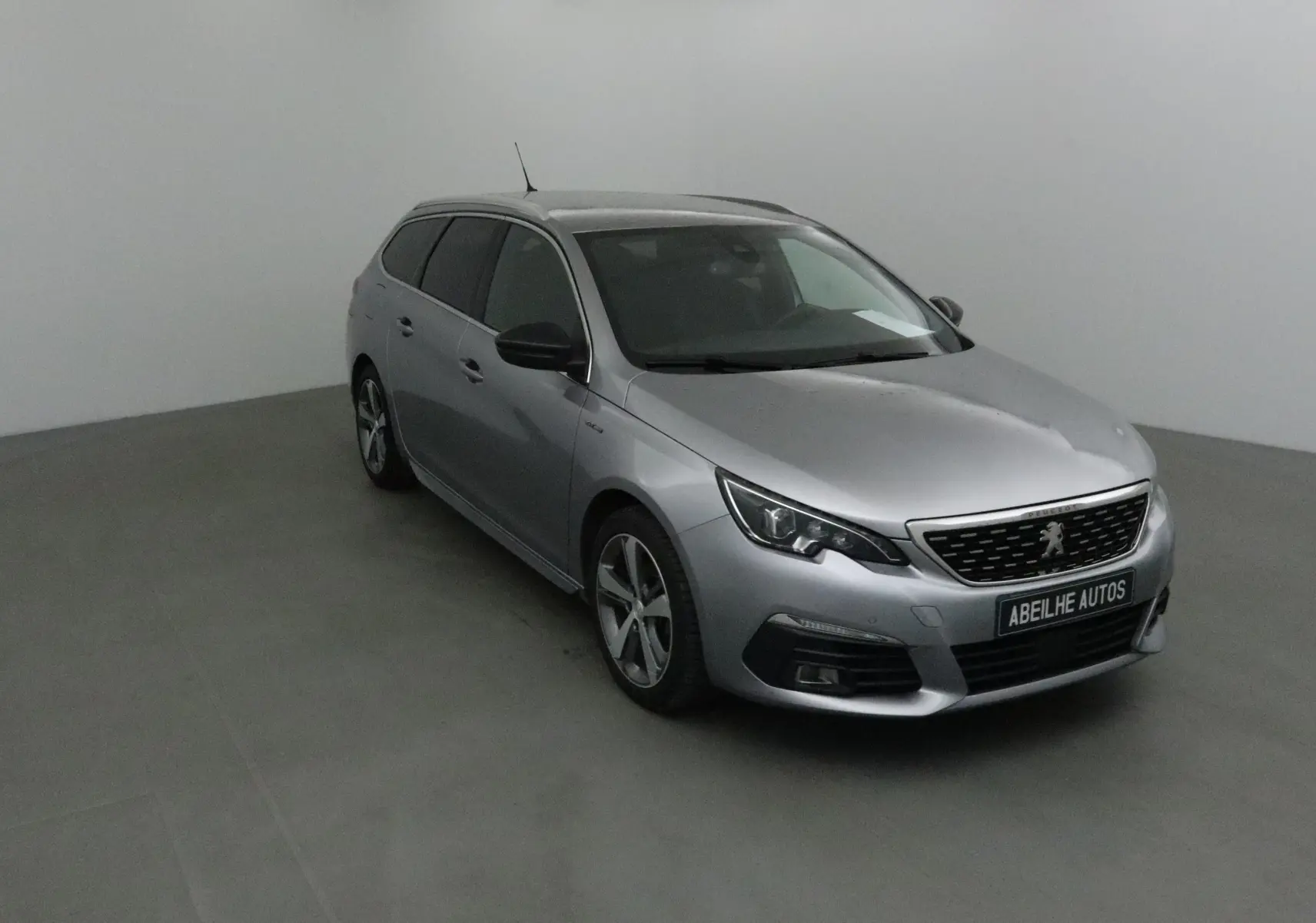 Peugeot 308 SW gris Artense vue 3/4 avant droit, avec jantes alliage et calandre noire distinctive.