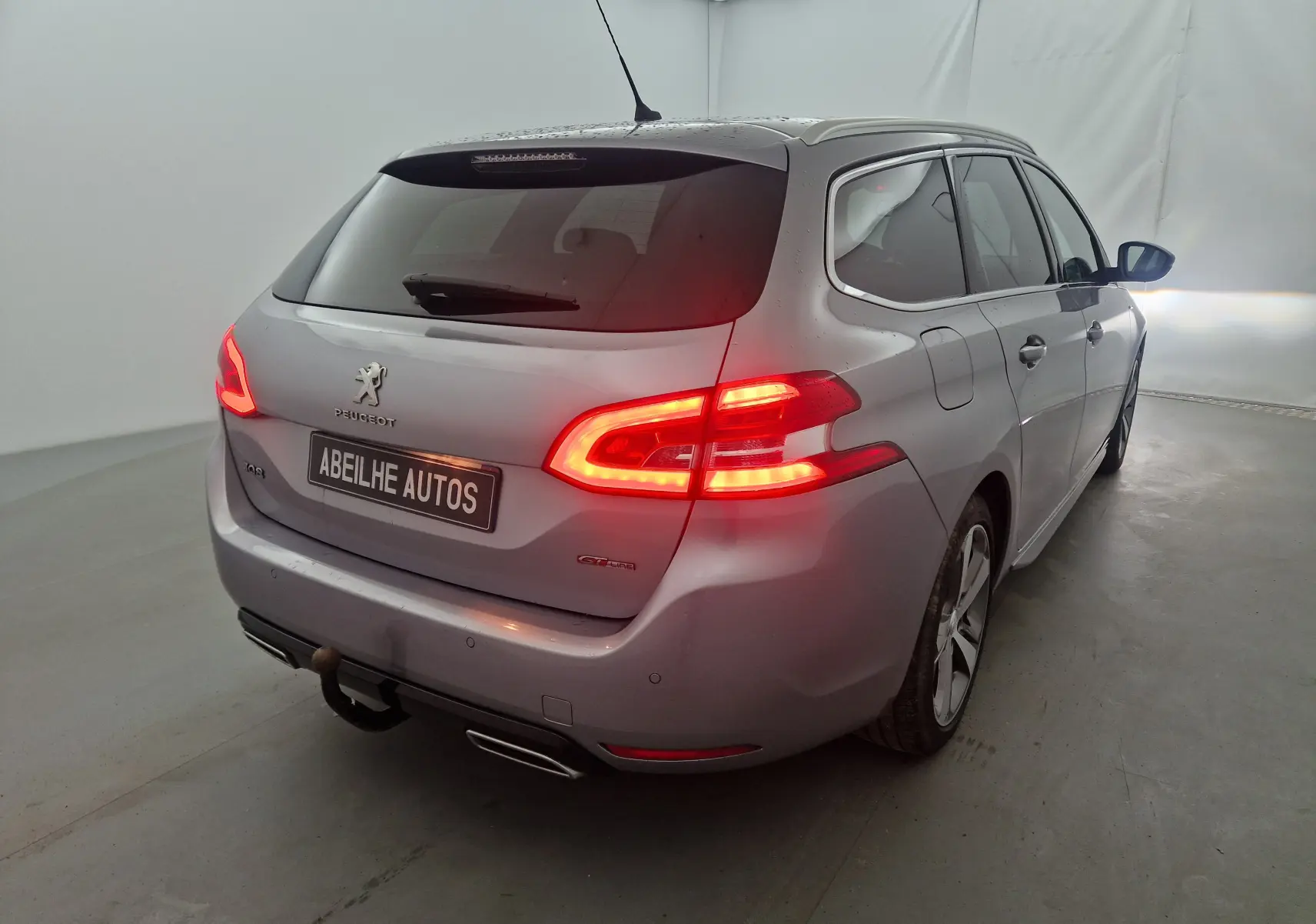 Peugeot 308 SW gris Artense vue 3/4 arrière droit avec feux allumés et attelage visible en studio.