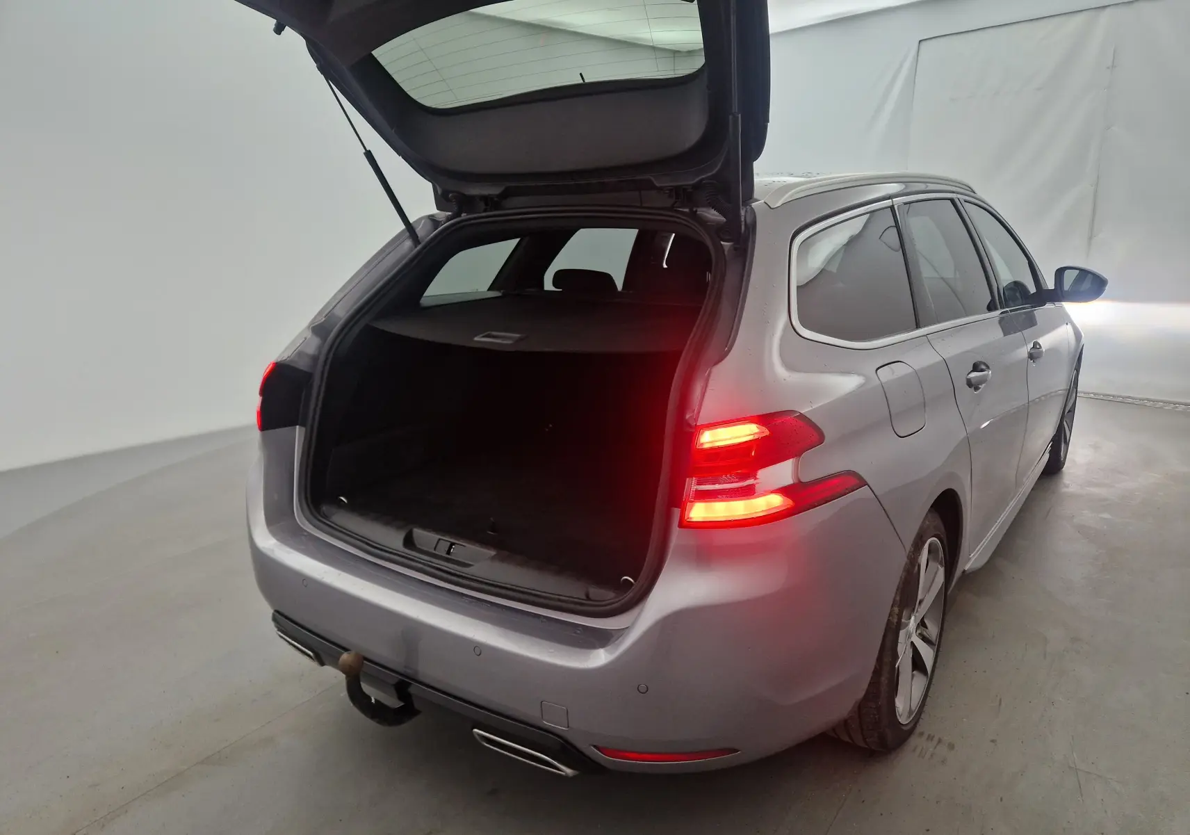Peugeot 308 SW gris Artense vue 3/4 arrière droit avec coffre ouvert et feux arrière allumés dans un studio.