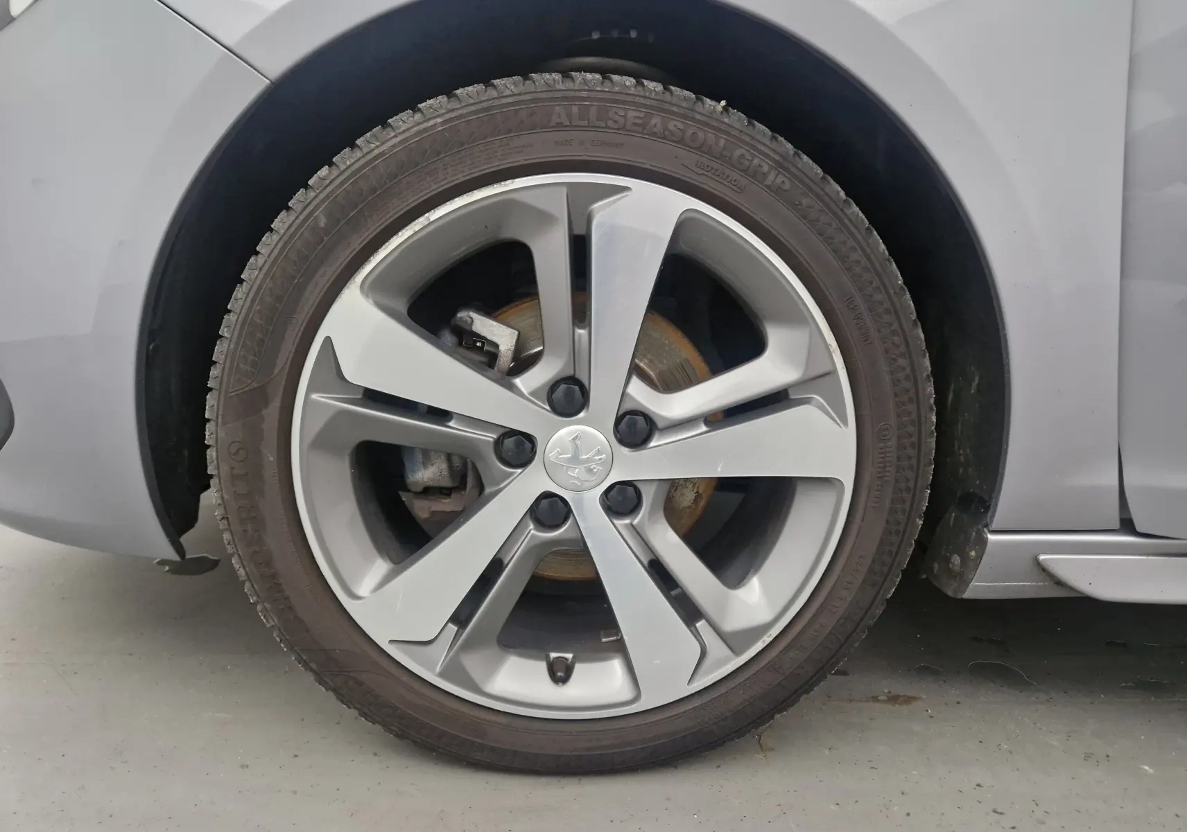 Gros plan sur la roue avant gauche d'une Peugeot 308 SW gris Artense, avec jante alliage 17 pouces et logo Peugeot central.